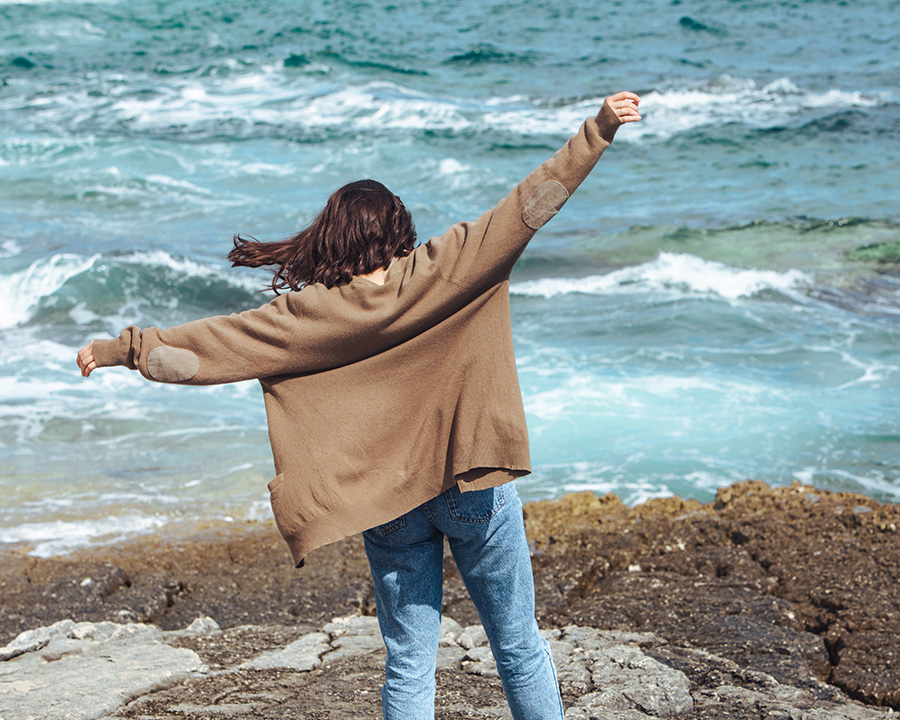 Woman stretching out her arms in front of ocean on Rockaway Beach in Pacifica, CA